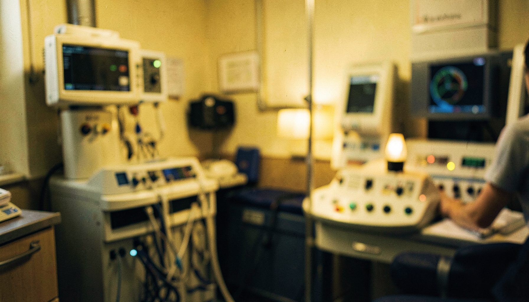 A healthcare setting with medical equipment in soft focus, warm amber and deep navy tones, conveying a serious and dedicated atmosphere.
